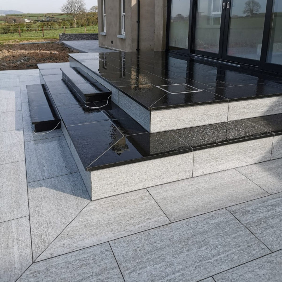 Patio area in Pietra Di Bagnolo porcelain paving tiles leading up to steps in a black porcelain paving. 