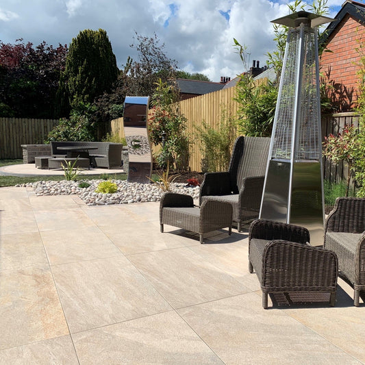 Patio area with wicker garden seats, heater and garden seating area in the background. Paving is Pietra Di Barge porcelain tiles. 