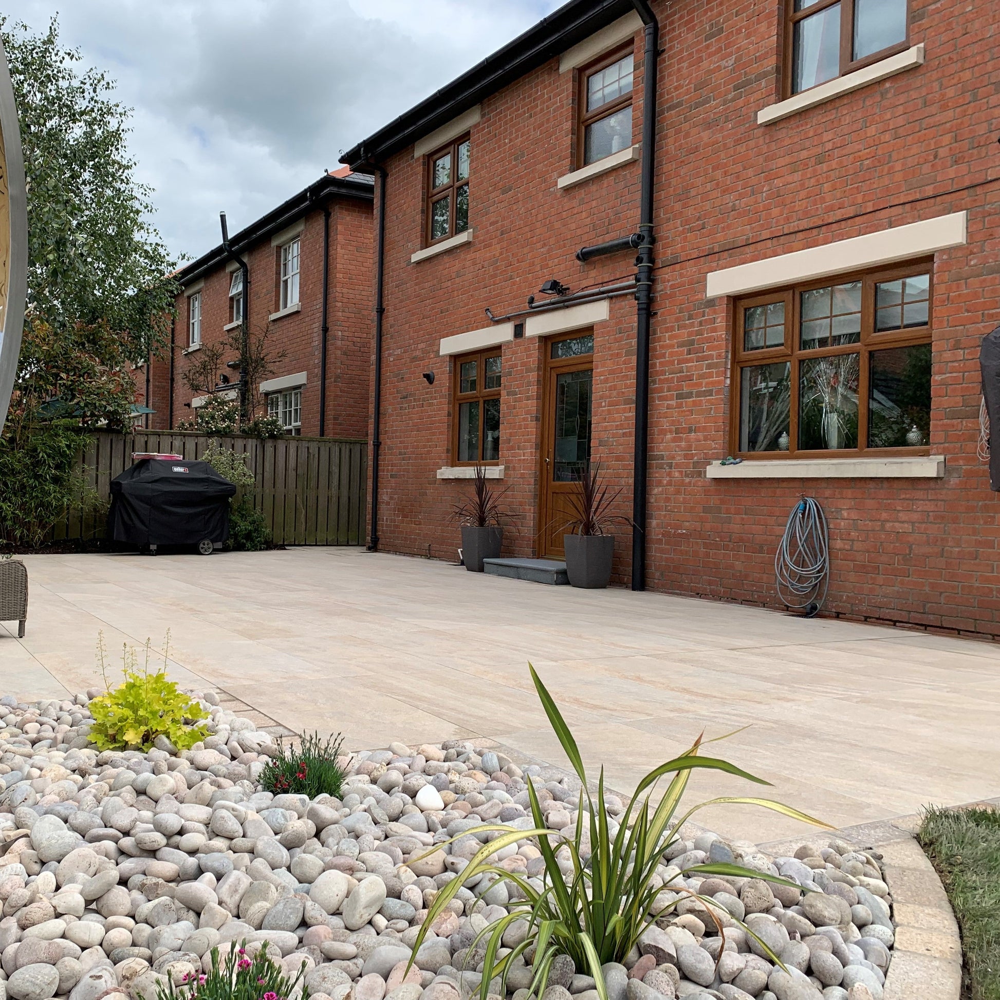 Patio area looking onto a red brick house. Paving is Pietra Di Barge porcelain tiles. 