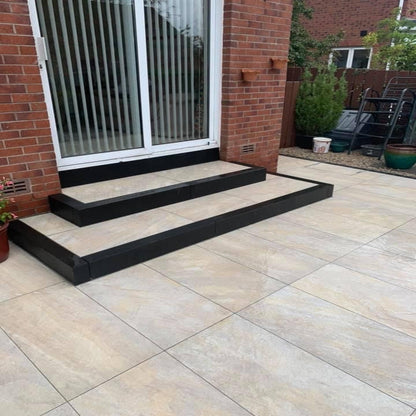 Rectangular beige porcelain paving tiles installed on the patio area  with a brick wall and window in the background. Paving is Pietra Di Barge porcelain tiles.