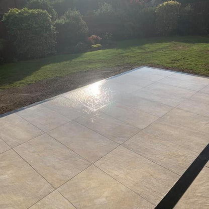 Patio area completed using Pietra Di Barge porcelain tiles. Garden and mature hedging in the background. 