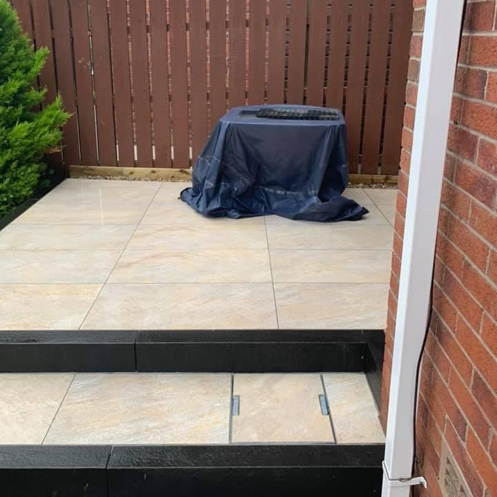 Small patio area completed using Pietra Di Barge porcelain tiles. Brown fence in the background. 