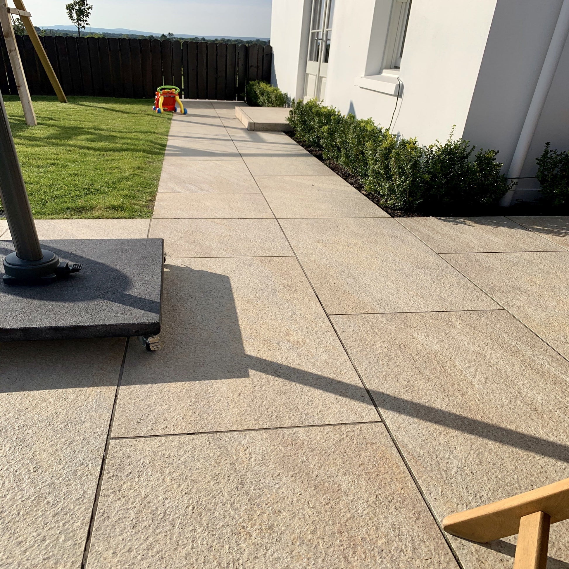 An outdoor installation of Pietra di Barge porcelain paving in a garden setting, showing rectangular beige tiles with a smooth finish.