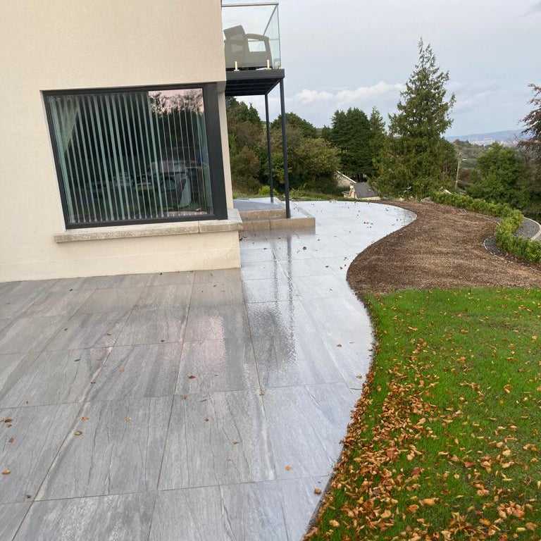 Pietra Di Vals Porcelain Paving Tiles installed on a curved patio area outside a modern hose with balcony.