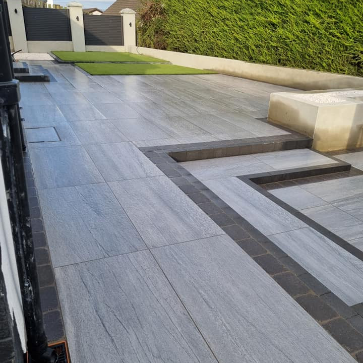 Large patio featuring Pietra Di Vals Porcelain Tiles with hedging and fence in the background.