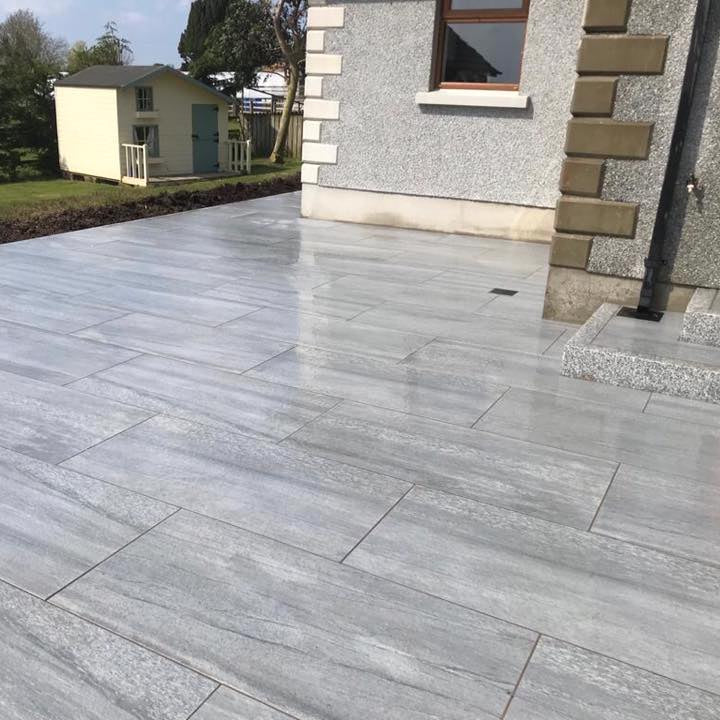 Large patio area featuring Pietra di Vals porcelain tiles. Garden and children's playhouse in the background. 