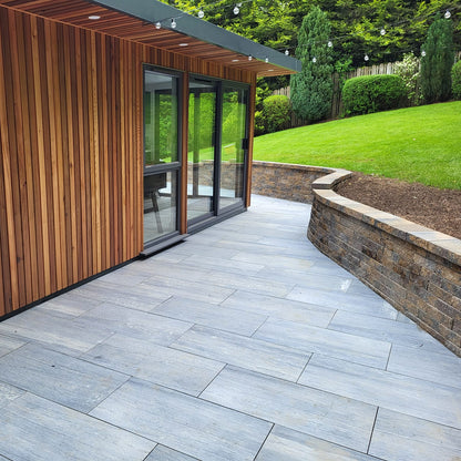 Patio area with stone wall and wooden cladded house. Paving is Pietra di Vals porcelain tiles.