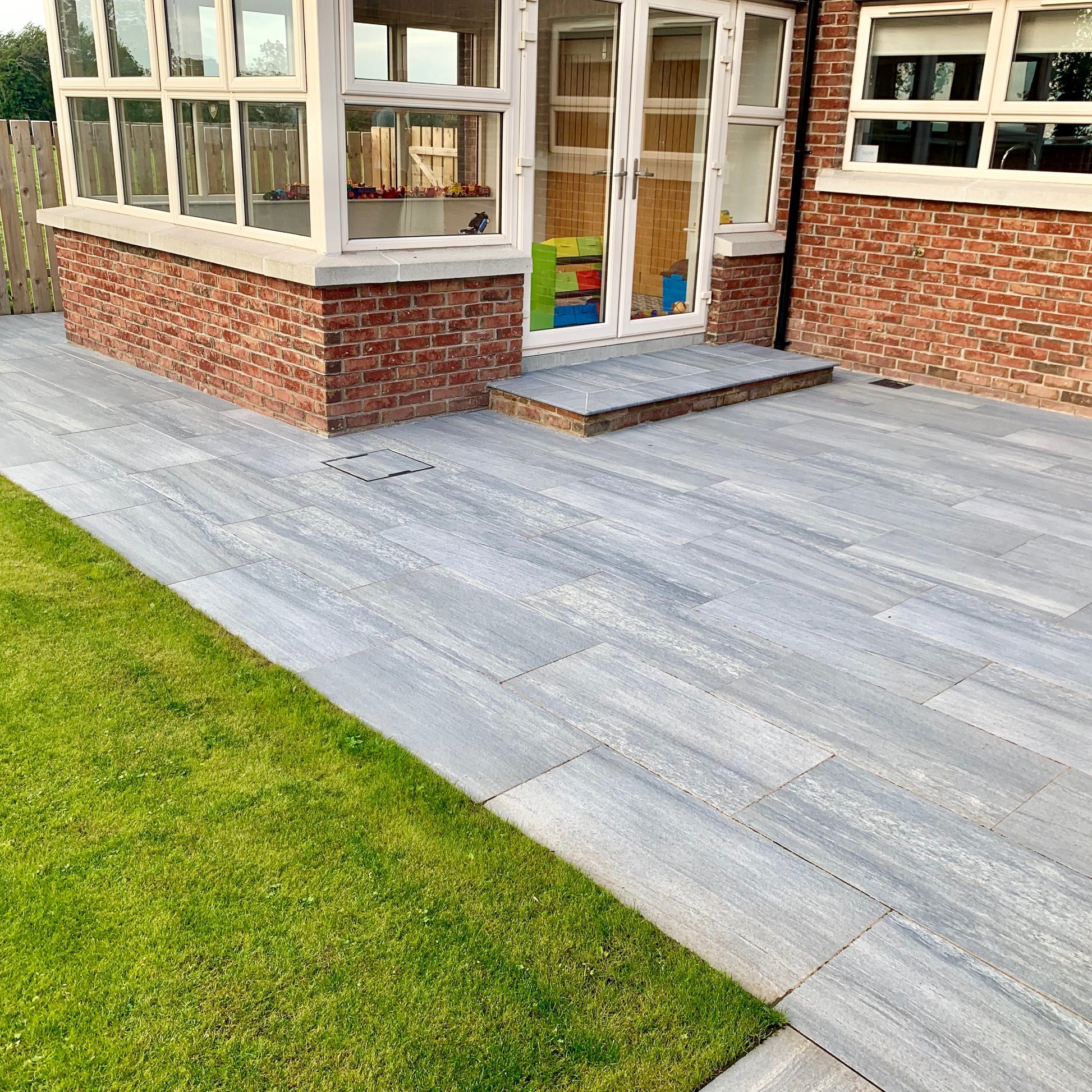 Garden patio area with step leading up to sunroom. Paving is Pietra di Vals porcelain tiles.