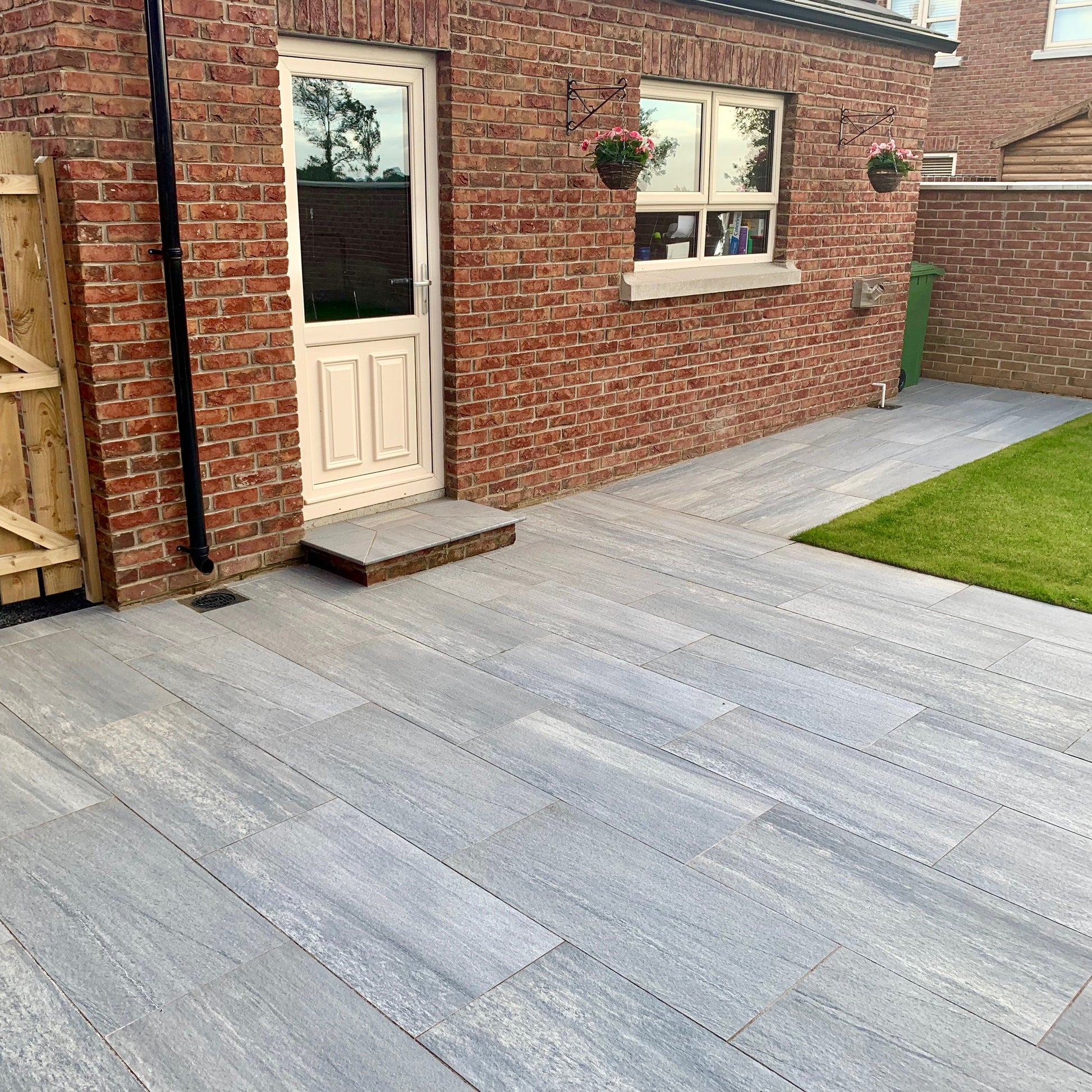 Patio area with step leading up to a red brick shed. Paving is Pietra di Vals porcelain tiles.