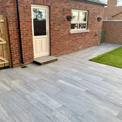 Patio area with step leading up to a red brick shed. Paving is Pietra di Vals porcelain tiles.