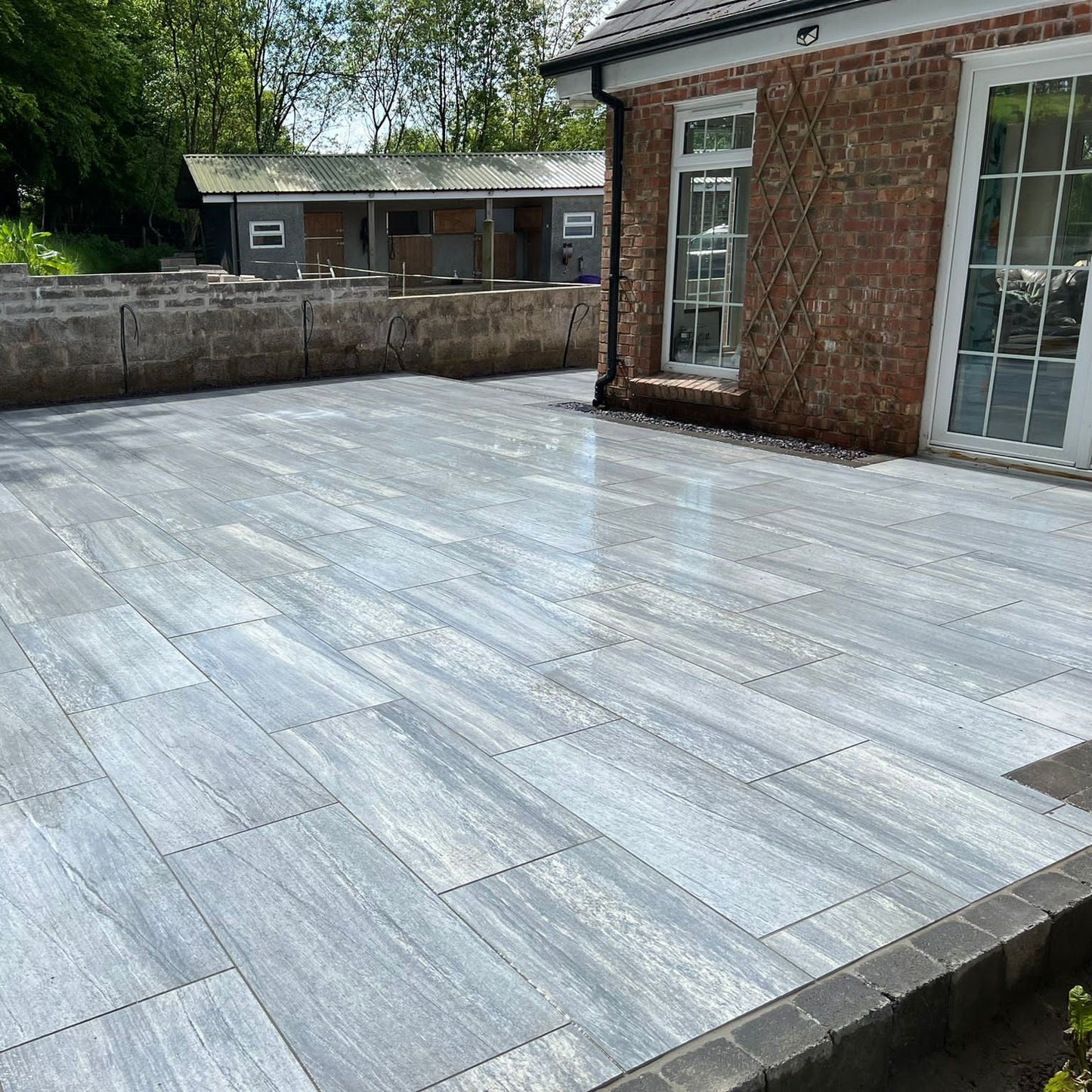 Large patio completed using Pietra di Vals porcelain tiles in 900 x 450 x 20mm size. Red brick house and horse stables in the background. 