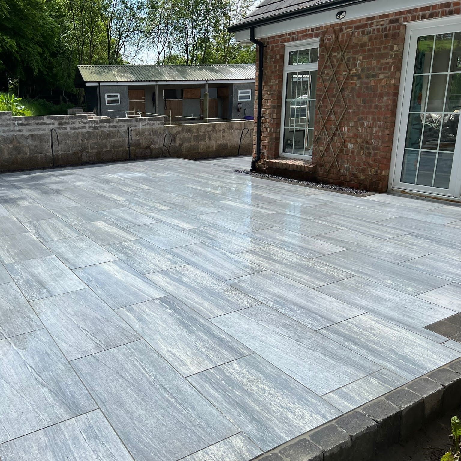 Large patio completed using Pietra di Vals porcelain tiles in 900 x 450 x 20mm size. Red brick house and horse stables in the background. 