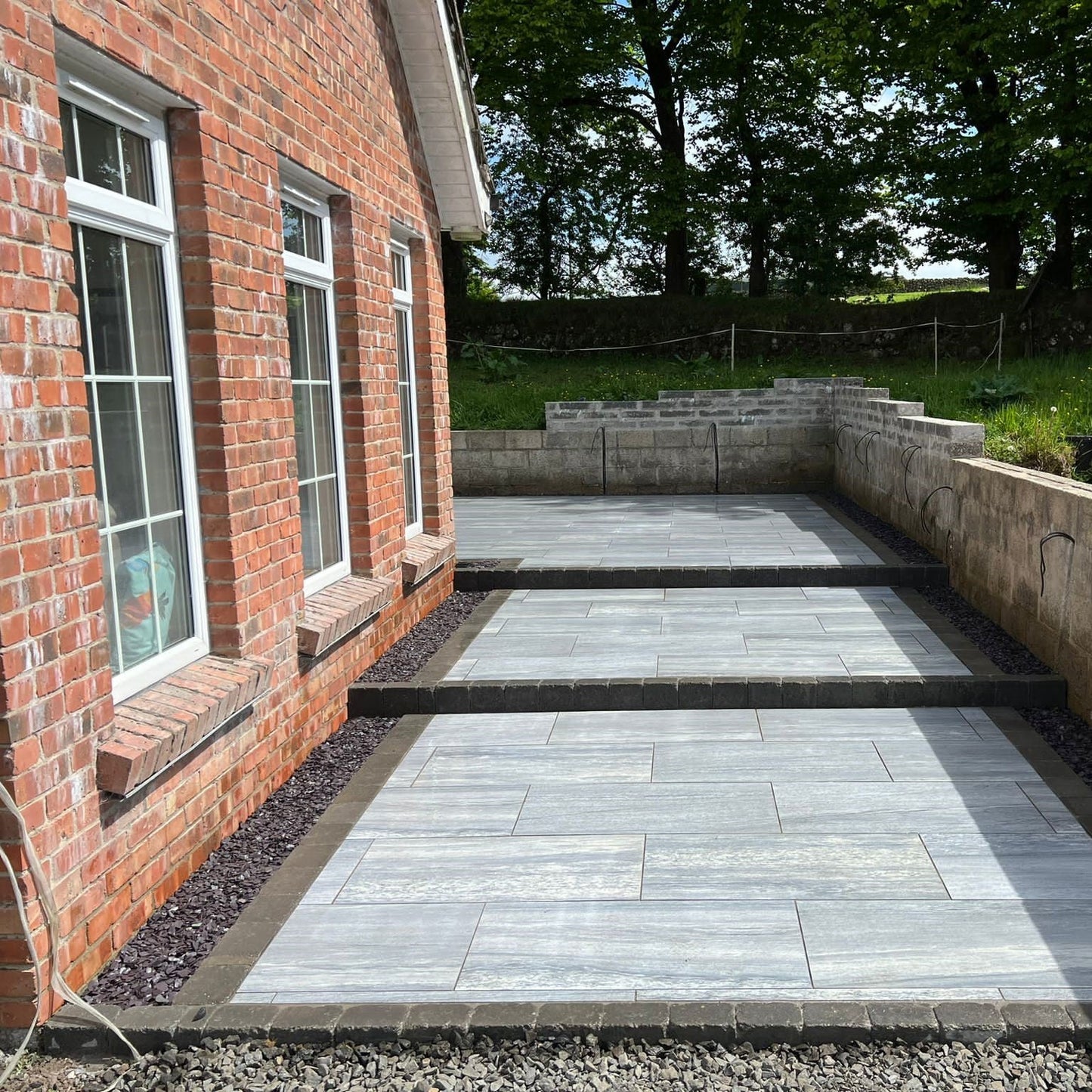 Patio area to the side of red brick house completed using Pietra di Vals porcelain tiles.
