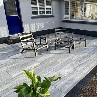 Patio area outside grey house with blue door. Paving is Pietra di Vals porcelain tiles. 