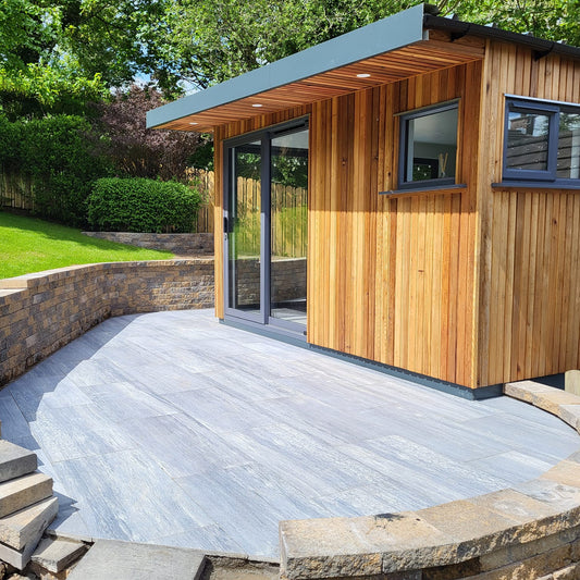 Modern wooden cabin with a stone patio and greenery. Paving is Pietra di Vals porcelain tiles.