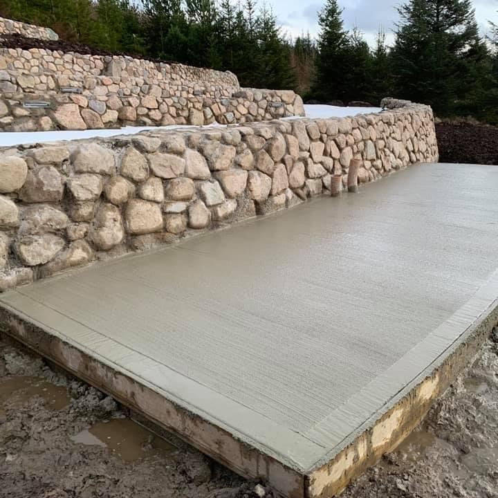 Concrete platform by a stone wall completed using Pink Sperrin Granite Mix Rockery with trees in the background