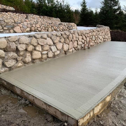 Concrete platform by a stone wall completed using Pink Sperrin Granite Mix Rockery with trees in the background