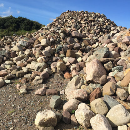 Heap of multi-coloured stones under a clear blue sky. Stones are pink Sperrin granite mix rockery stones.