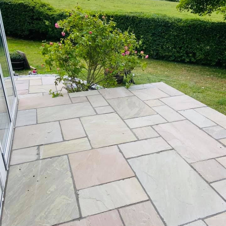 Paved patio area featuring Raj Green Sandstone Paving with a garden and trees in the background. 