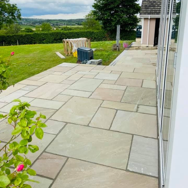 Paved patio area featuring Raj Green Sandstone with grass and trees in the background. 