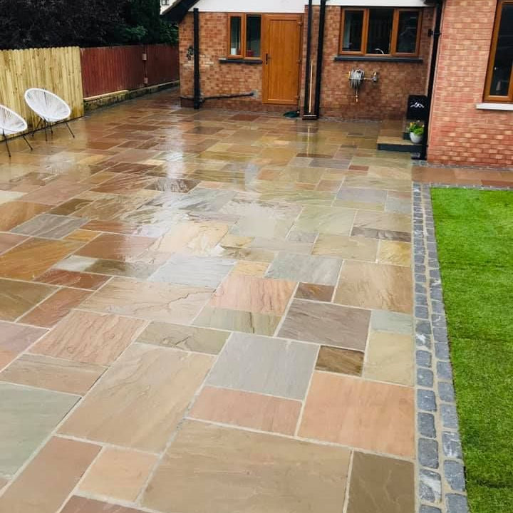 Paved patio area in front of a house with a grassy lawn. Paving is Raj Green Sandstone patio packs. 