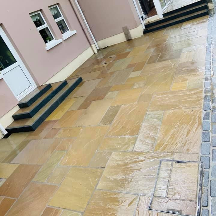Paved patio area in front of a house with a pink exterior. Paving is Raj Green Sandstone. 