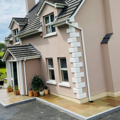 Two-story house with a Pink exterior and grey roof, featuring a small patio area with plants and pathway completed using Raj Green Sandstone. 