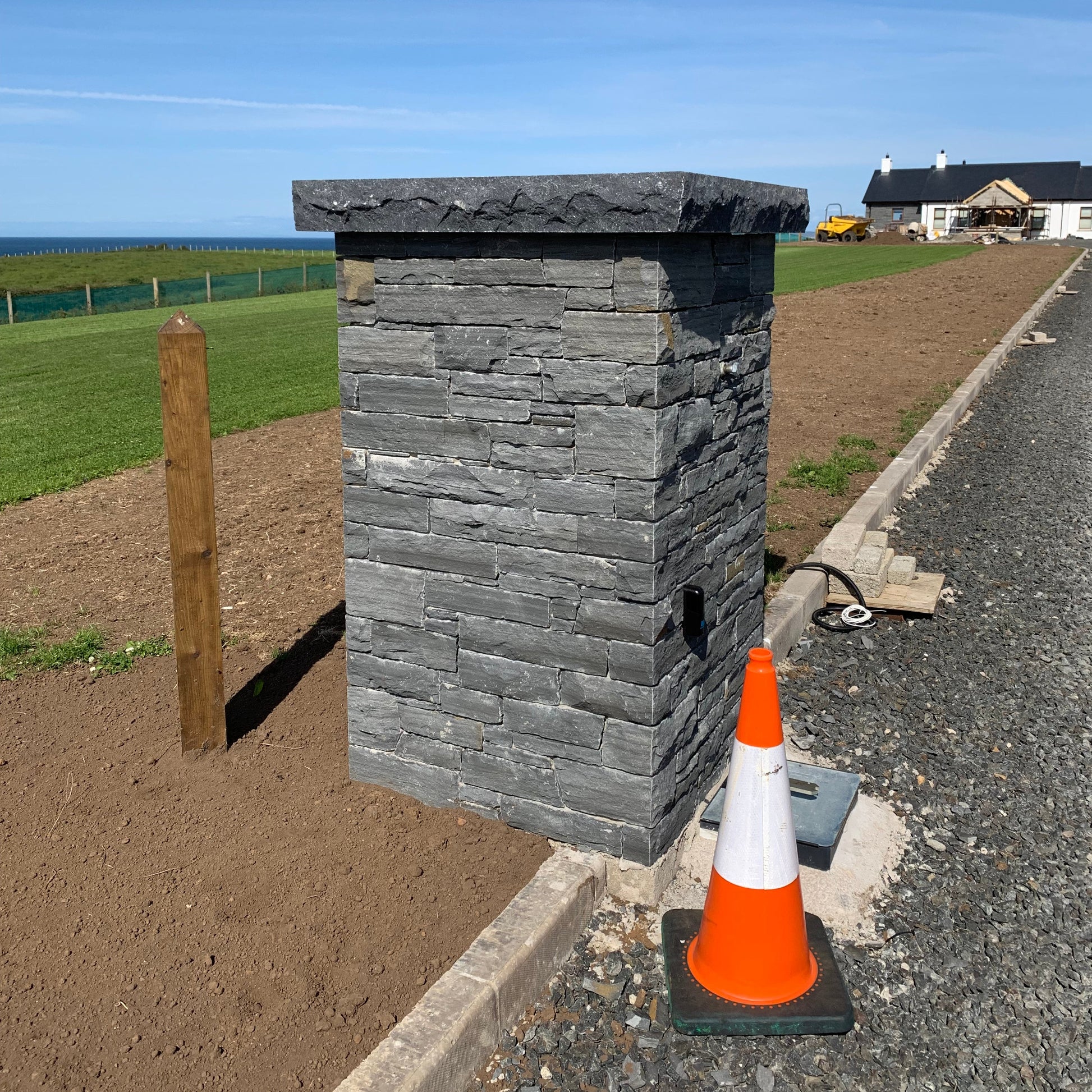 Stone pillar on a road with an orange traffic cone and a clear blue sky. Bespoke blue limestone pillar cap with rockfaced finish. 