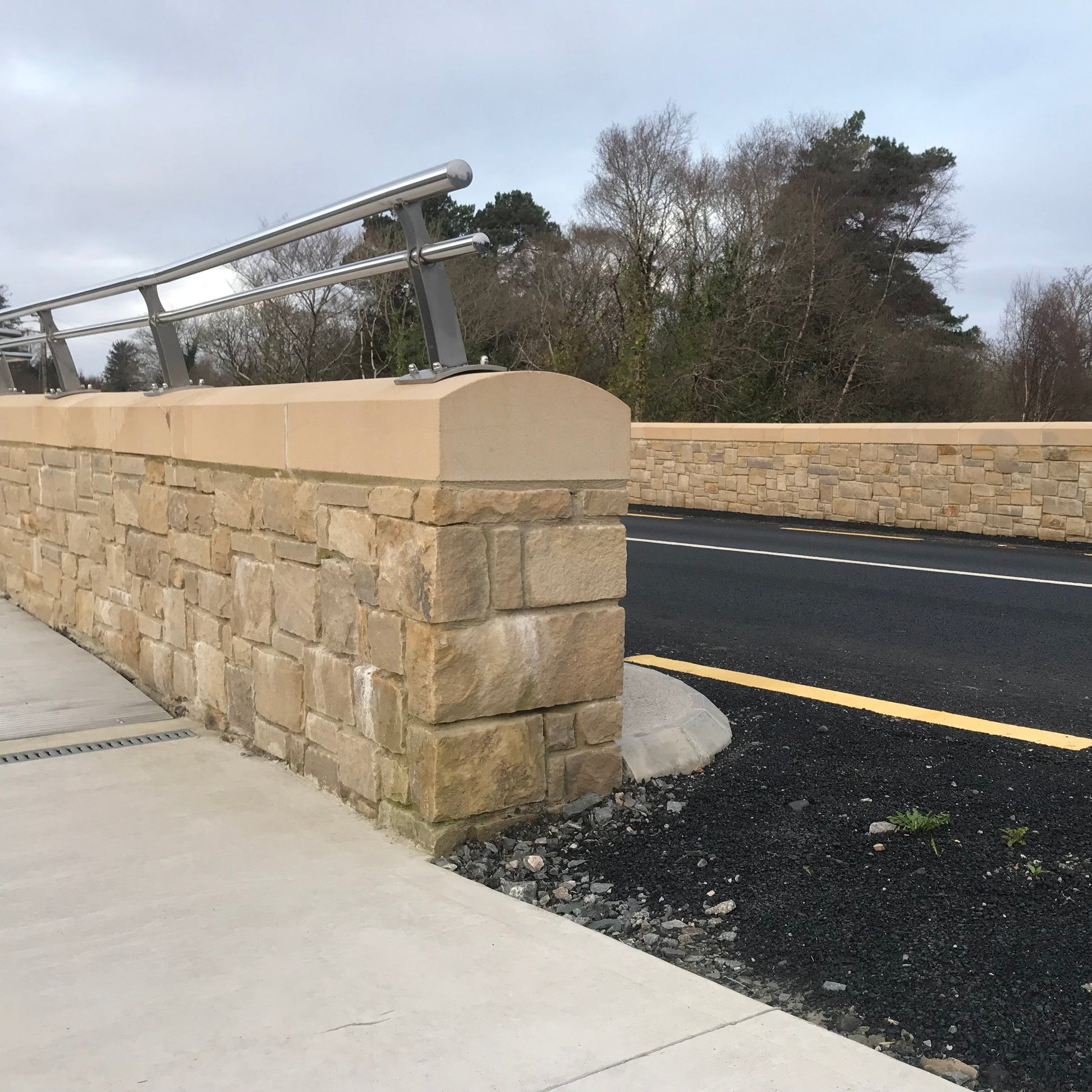 Roadside stone wall with railing fixed on top of bespoke sandstone wall capping. 