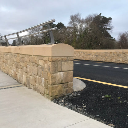 Roadside stone wall with railing fixed on top of bespoke sandstone wall capping. 