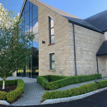 Large architectural building with large glass windows with smaller windows featuring bespoke sandstone lintels and sills. 