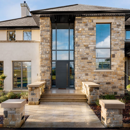 Modern house exterior with stone façade and large glass windows featuring a bespoke sandstone lintel and sill. 