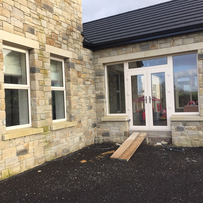 Stone building with a black roof and windows, including a double door entrance featuring bespoke sandstone lintels and sills.