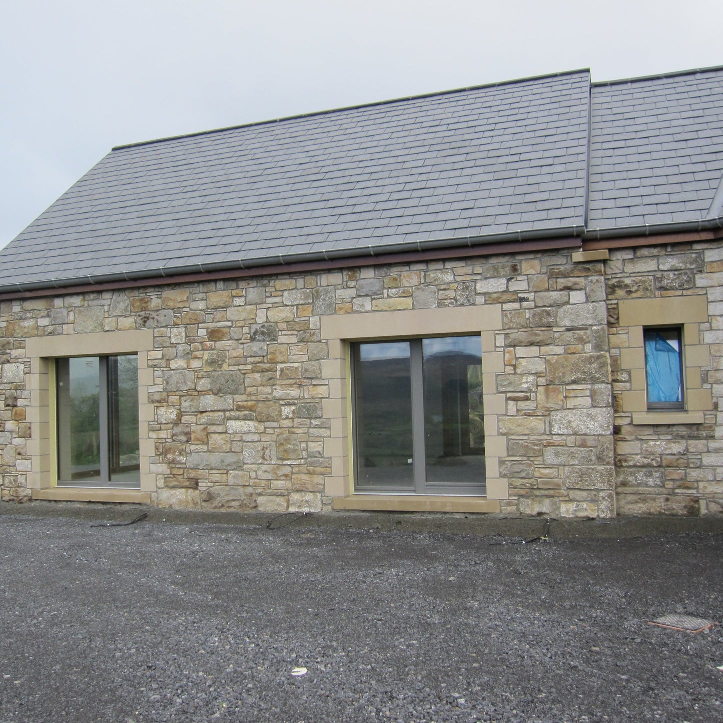Stone-built house with large doors and a grey roof on a cloudy day. House features sandstone lintels and quoins. 