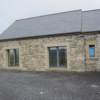 Stone-built house with large doors and a grey roof on a cloudy day. House features sandstone lintels and quoins. 