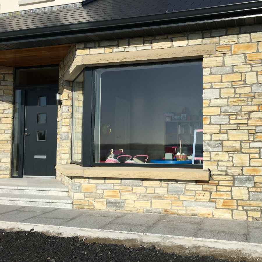 Stonework exterior of a building with large window featuring a bespoke sandstone window lintel and sill with a rockfaced finish. 