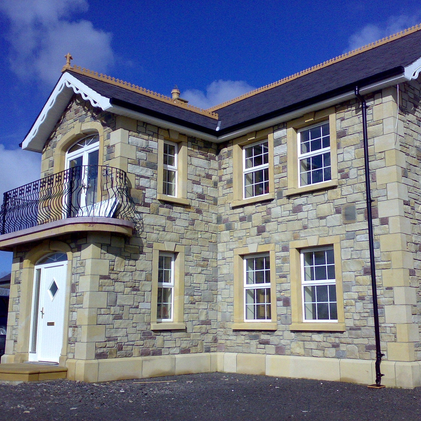 Stone house with a balcony and multiple windows under a blue sky with bespoke sandstone window surrounds, quoins and plinths. 