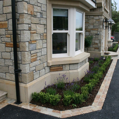 The image shows the lower part of a stone-fronted building with a classic architectural design, featuring a bespoke sandstone plinth with a planted area and a window. 