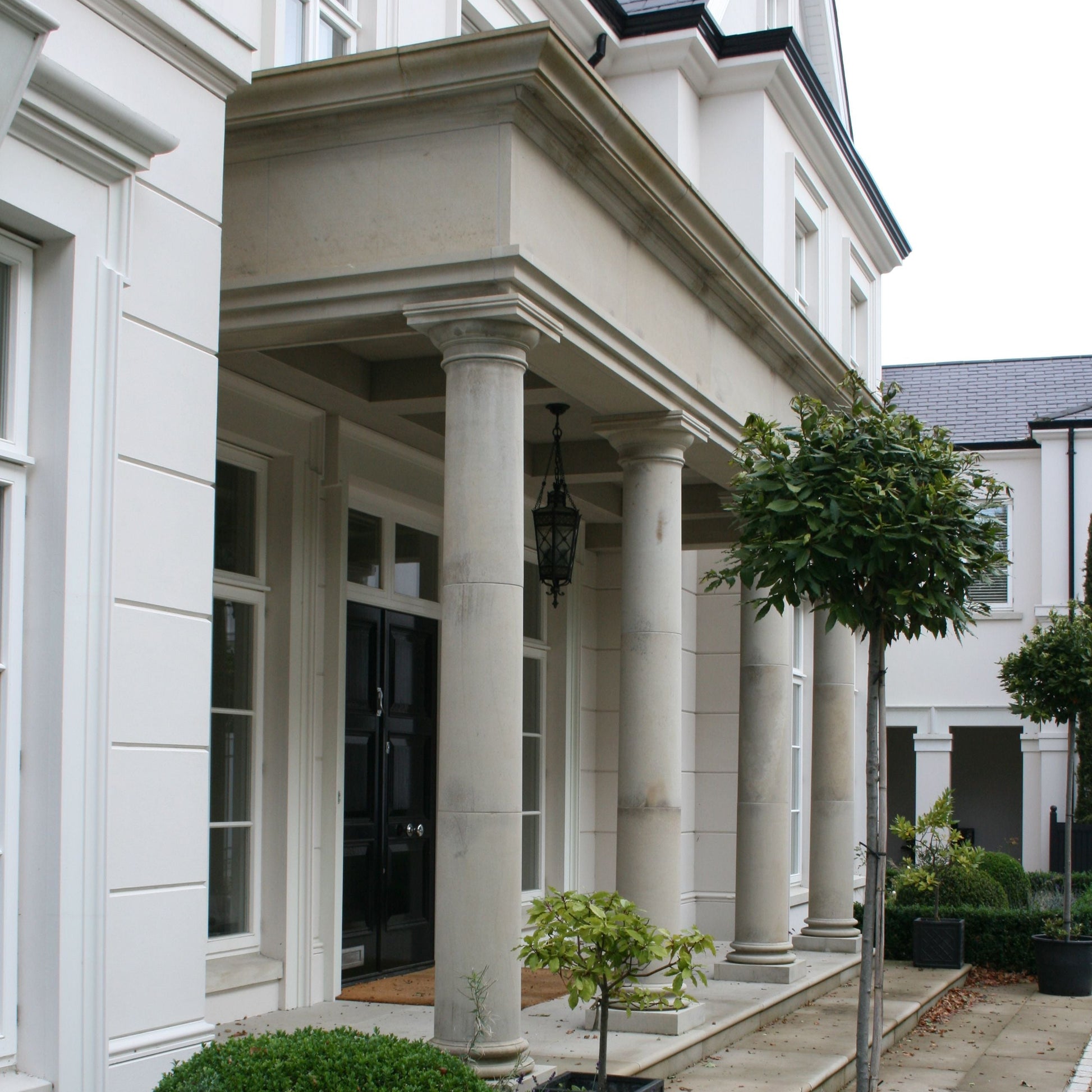 Bespoke Sandstone Portico on a grand home with a black front door and planting. 