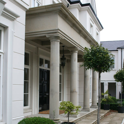 Bespoke Sandstone Portico on a grand home with a black front door and planting. 
