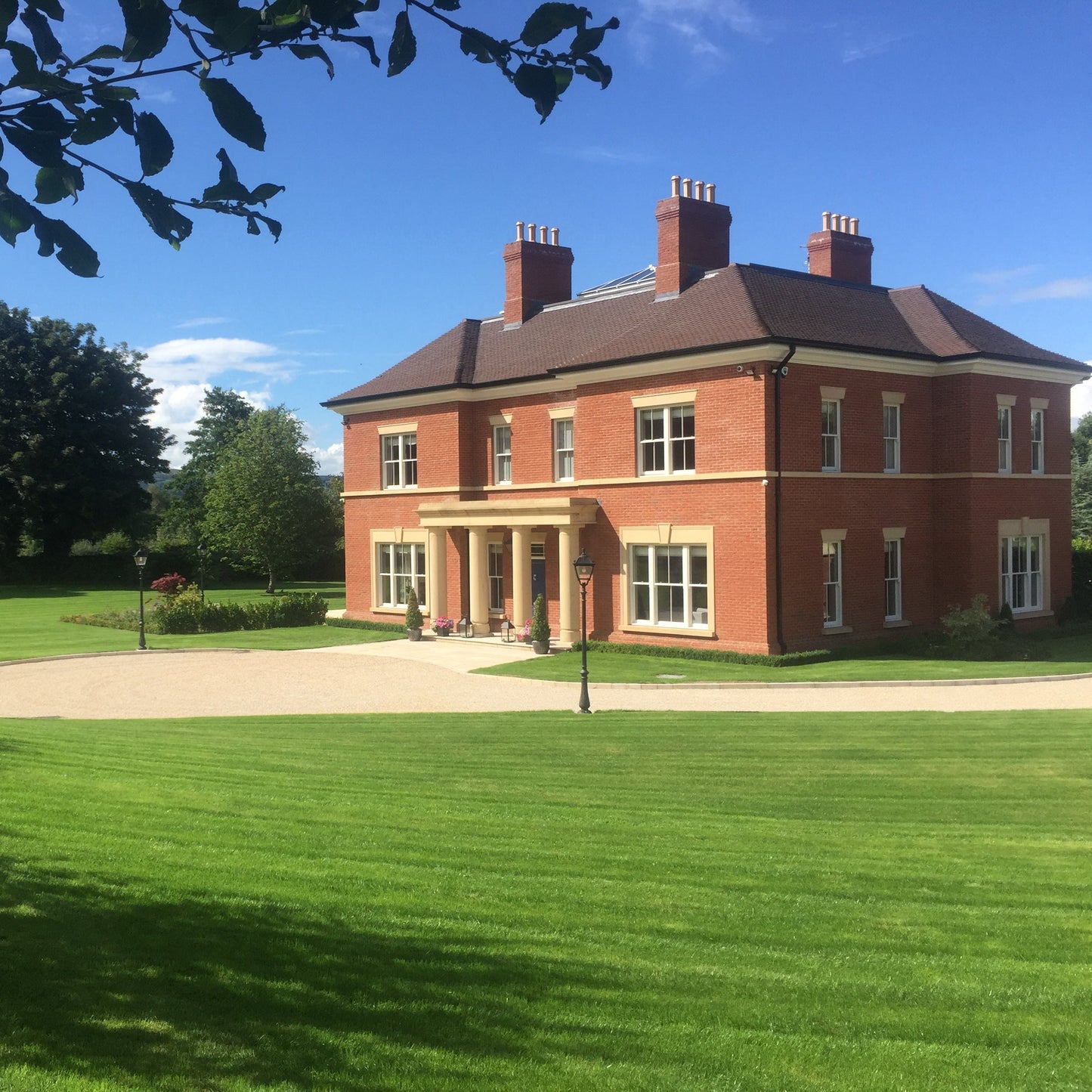 Large two storey red brick house with a sandstone portico and sandstone window surrounds and lintels. 