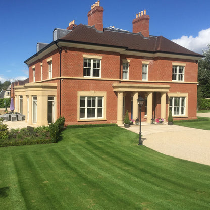 Large red brick mansion with bespoke sandstone portico and a well-manicured lawn and driveway.