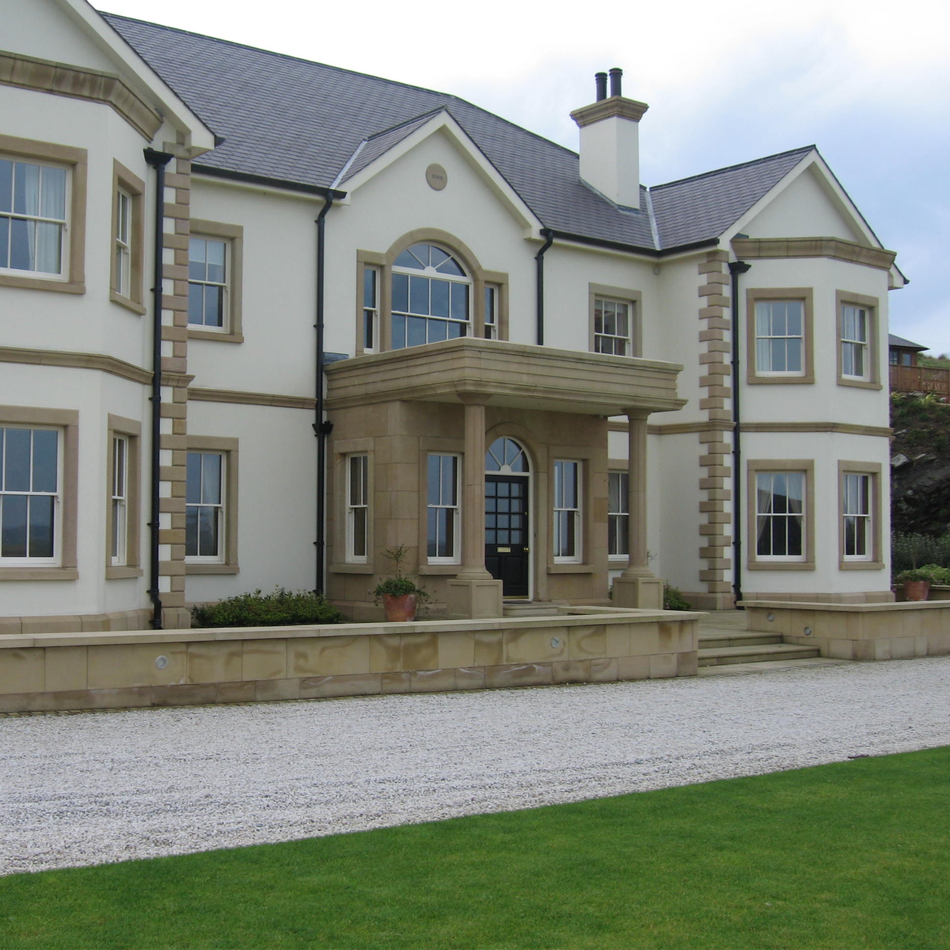 Large, elegant house with Sandstone Portico and a driveway with a well-maintained lawn.