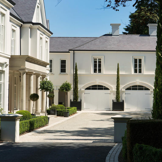 A traditional two-story house with a portico featuring columns and a pediment, in a sandy colour, complementing the architectural style of the building.