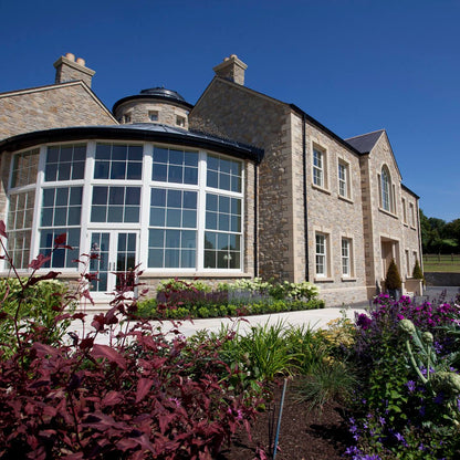 Large stone house with glass sunroom. House features bespoke sandstone quoins and window surrounds. 