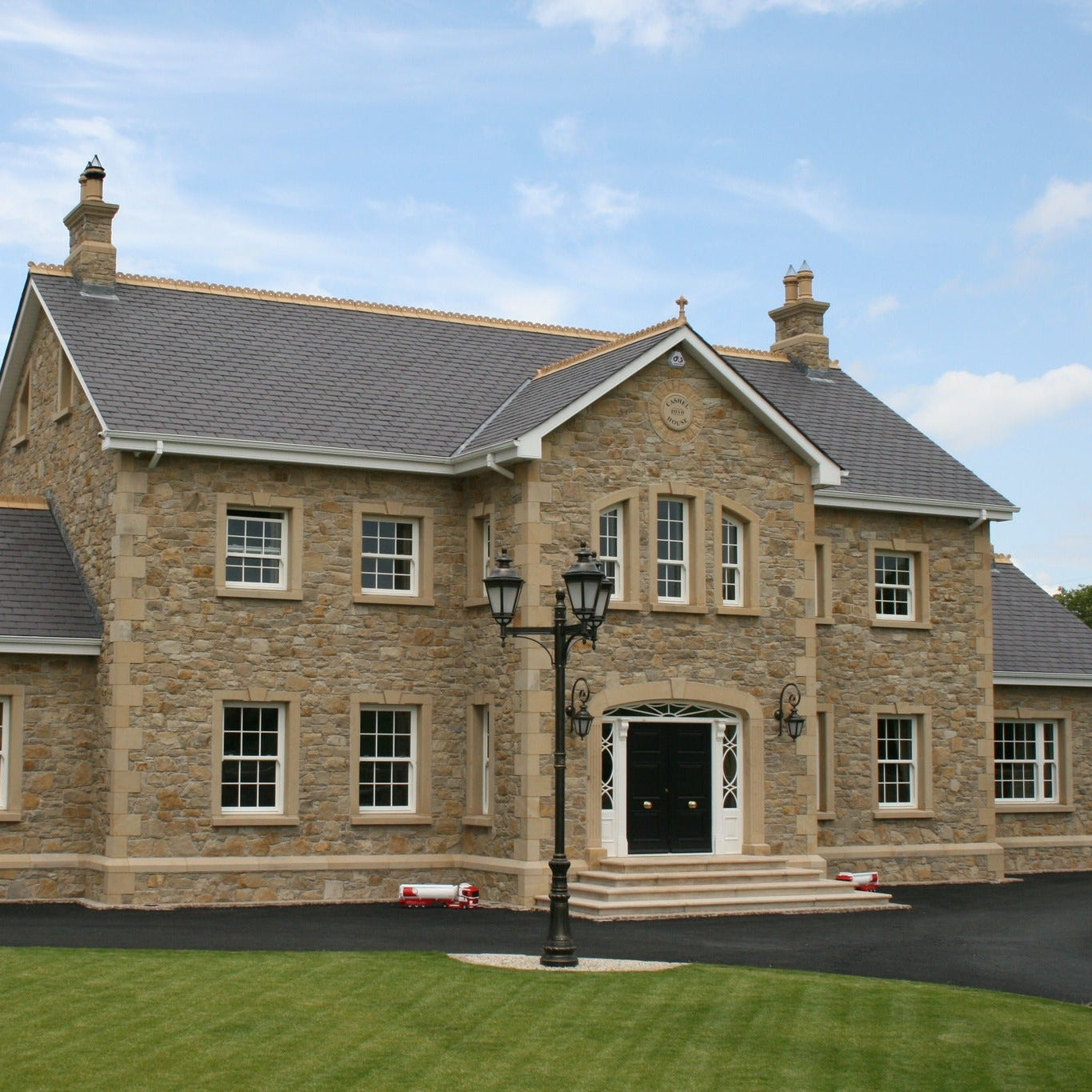 Large two storey stone house with architectural sandstone surrounds, steps, string course and quoins. 