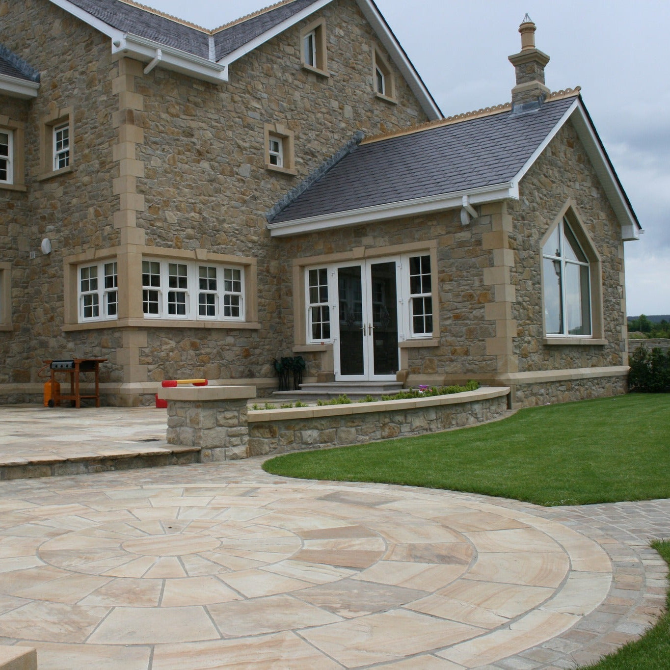 Back of stone house featuring architectural sandstone window surrounds, door surround, string course, wall capping, quoins and paving circle. 