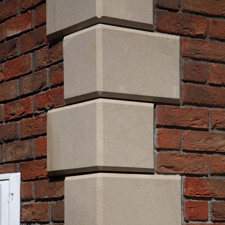 Close up of bespoke sandstone quoins on red brick building. 