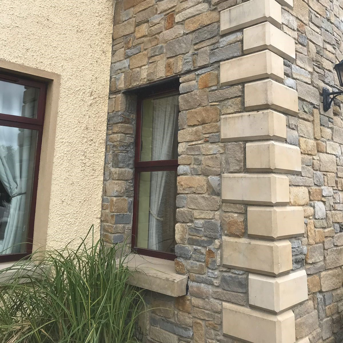 Stone façade of a building with windows and decorative bespoke sandstone quoins. 