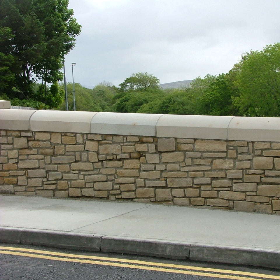 Stone wall with curved sandstone wall capping along a road with trees in the background
